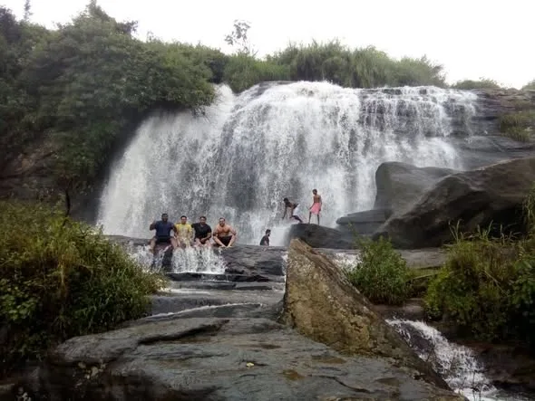 Visitors at a broad waterfall flowing over dark rocks in Kanthalloor